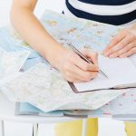 Eine Frau plant ihre Reiseroute auf einer Landkarte und macht sich Notizen