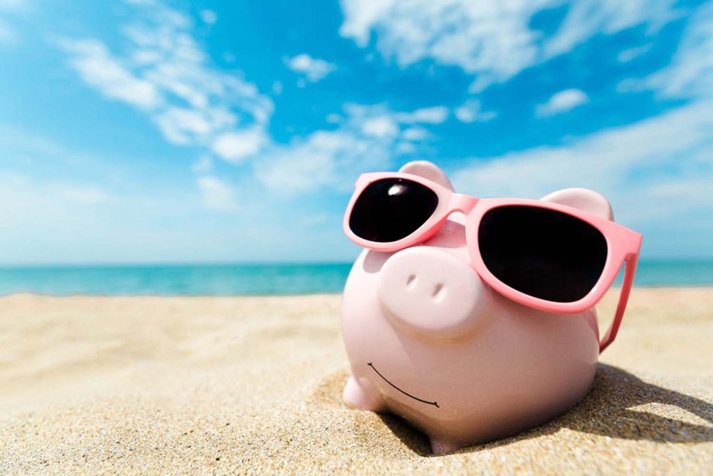 Ein Sparschwein liegt mit einer Sonnenbrille am Strand