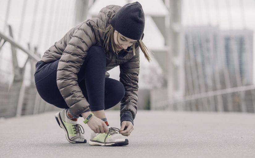 Warm angezogene Frau bindet sich ihren Schuh fürs Joggen