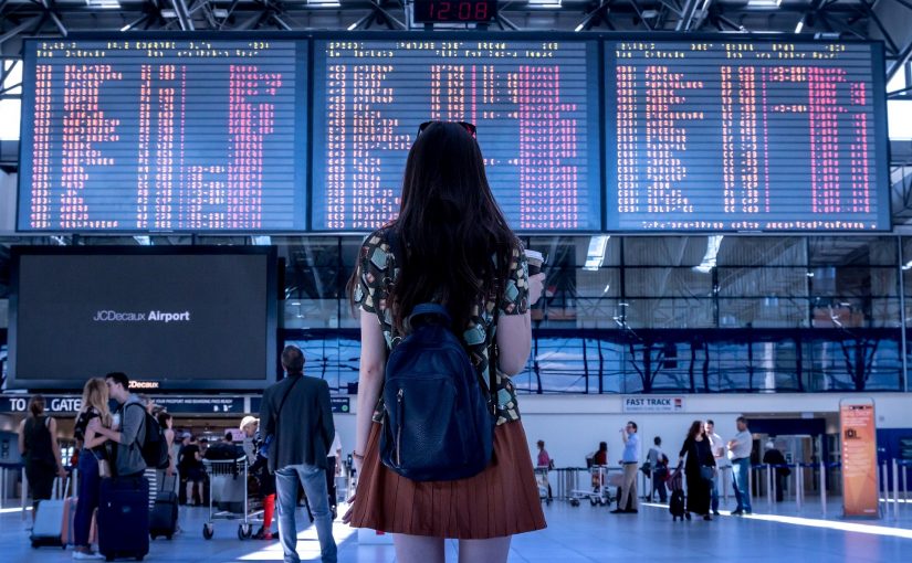 Eine Frau steht am Flughafen in einem Terminal und schaut auf eine riesige Leinwand, auf der die Flugzeiten angezeigt werden